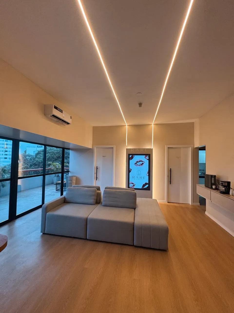 Sala de espera da RARE Clinic com iluminação linear, sofá e painel da marca